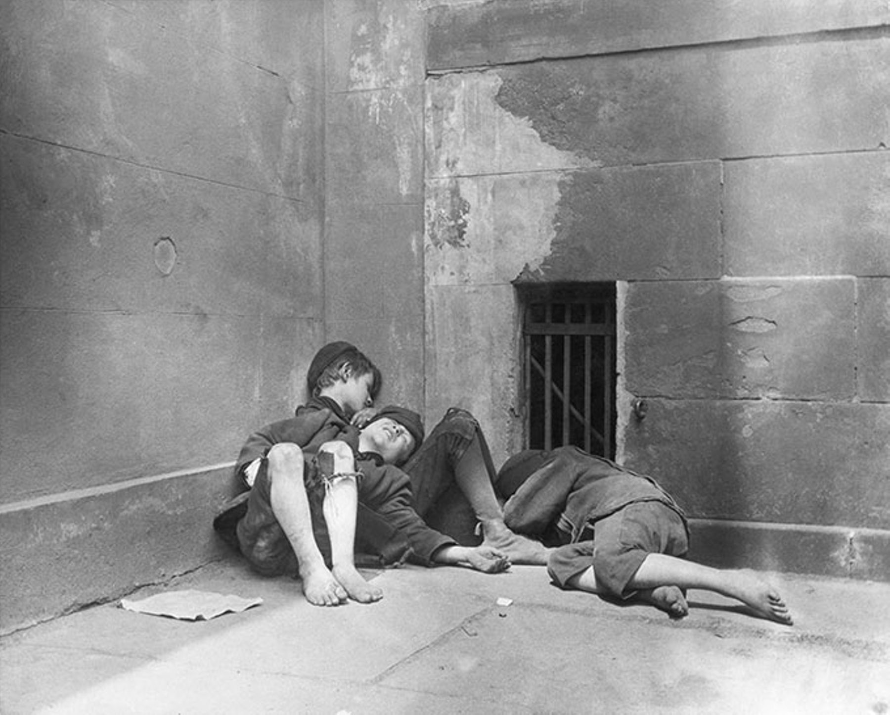 Homeless newsboys sleep huddled in a corner outside the Mulberry Street Church in Manhattan, ca. 1890.