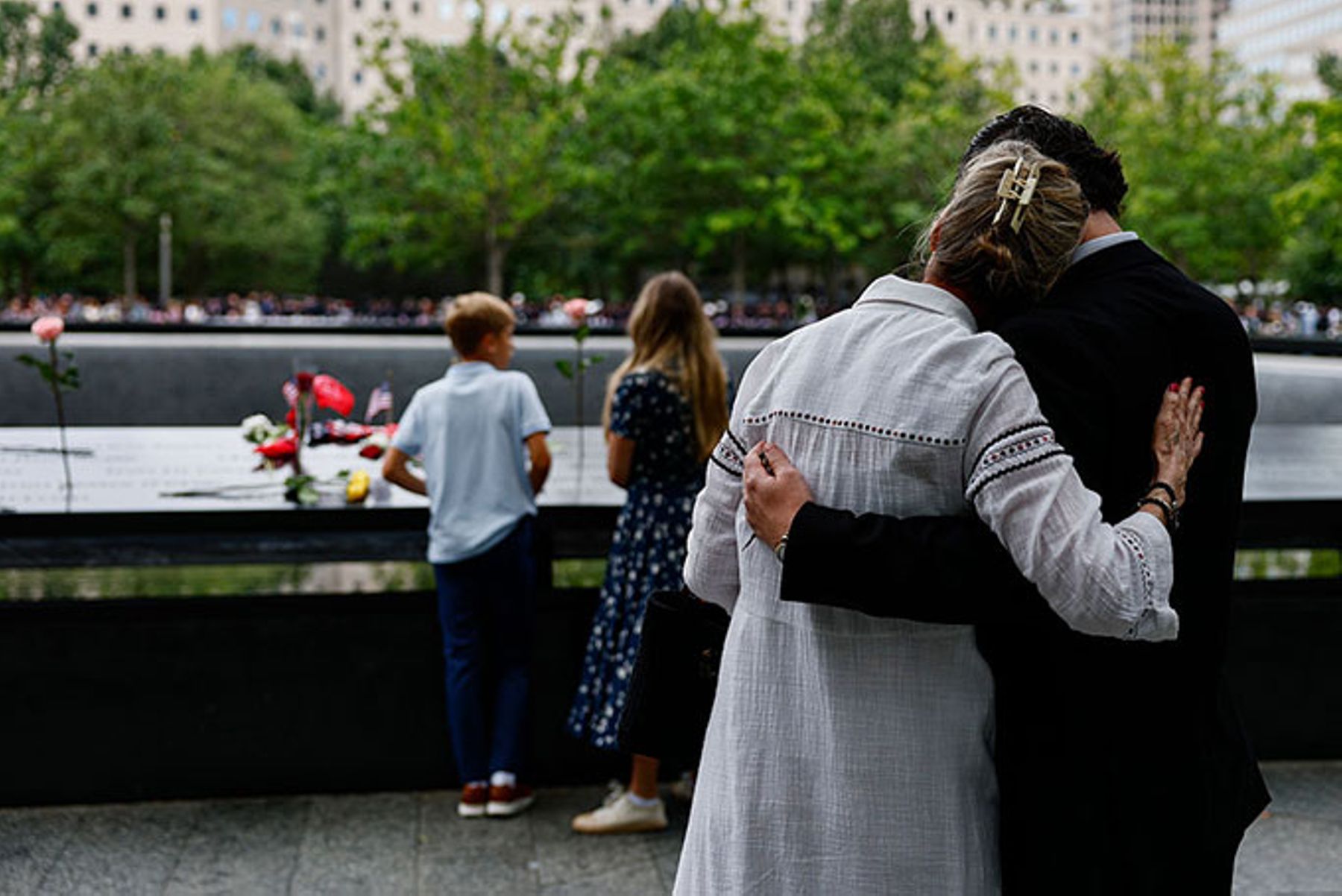Dean Toomey embraces Kerry Irvine standing near inscribed names in a reflecting pool at the 9/11 Memorial.